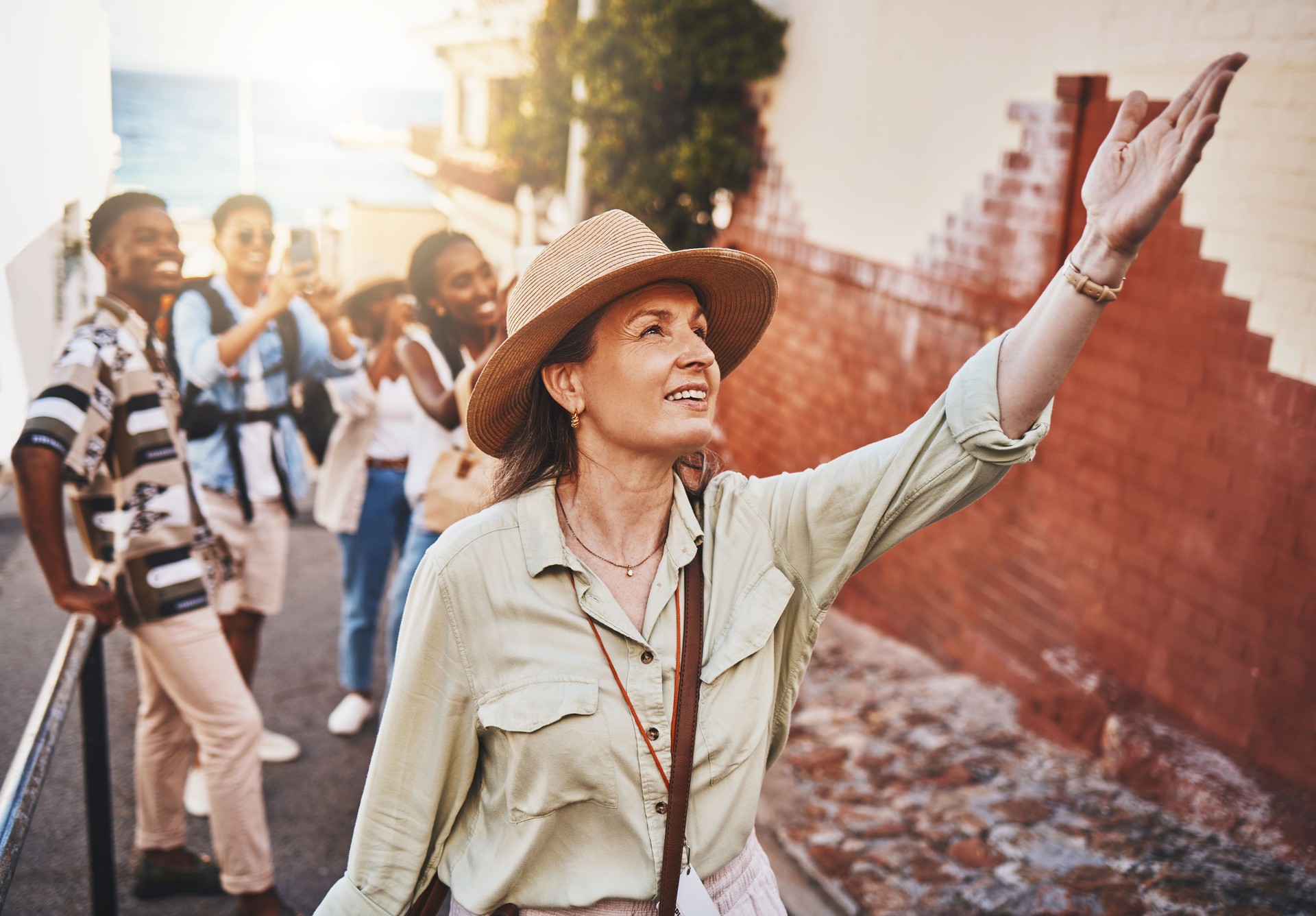 Travel, education and a guide with students on school field trip, on urban tour. Woman, city guide and group of happy tourists, pointing at local architecture and learning on international holiday.